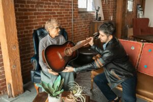 Homem tocando violão em casa à noite, demonstrando os benefícios de aprender violão para reduzir ansiedade e encontrar bem-estar emocional